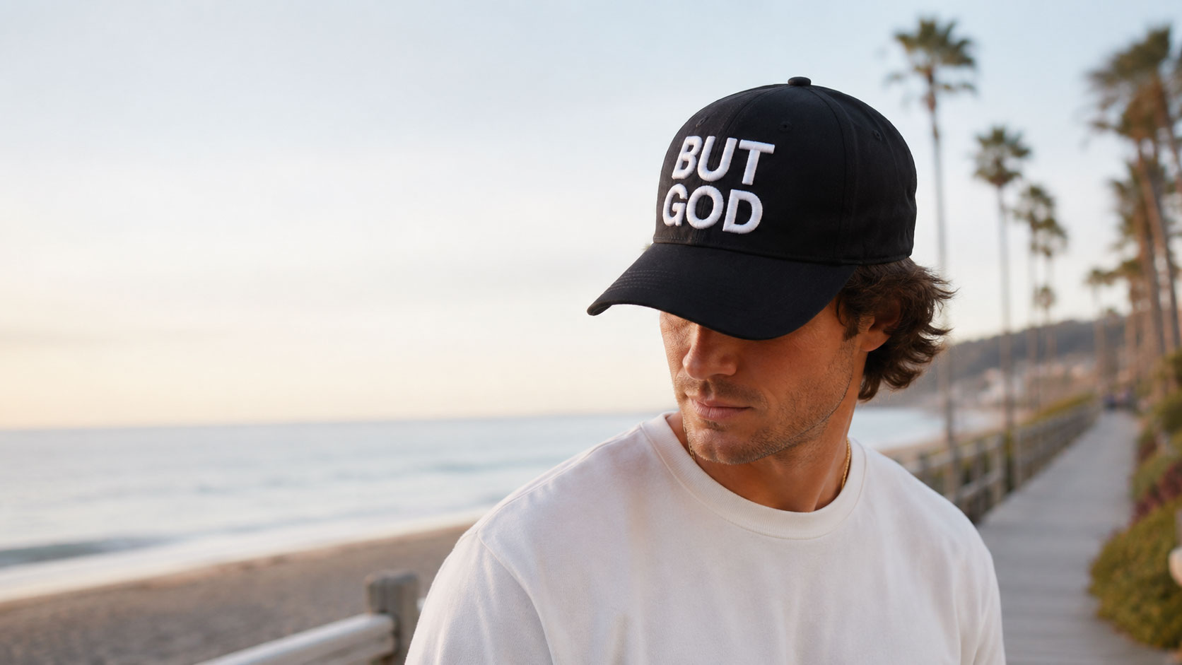 Model wearing the black But God hat by the beach at sunset
